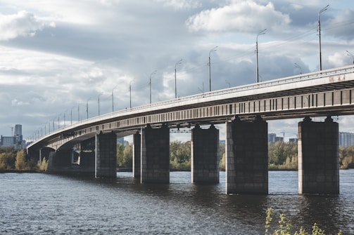 A large concrete bridge spanning a wide river with cranes in the background.