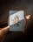 A playing card featuring a character resembling a robot is placed on a wooden surface. The robot design on the card appears in shades of orange, brown, and white. Light and shadow create a diagonal line across the card, adding contrast and highlighting its surface texture.