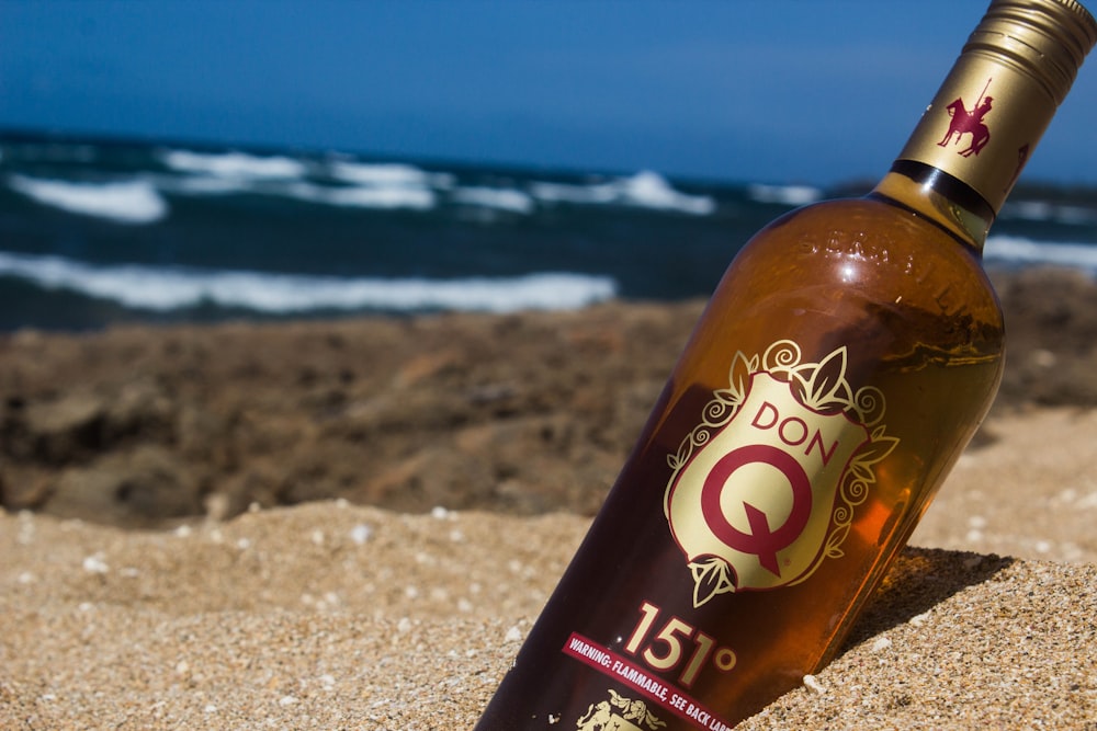 orange and white labeled bottle on beach sand during daytime