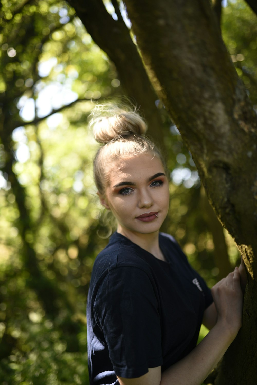 girl in blue crew neck shirt standing beside brown tree during daytime