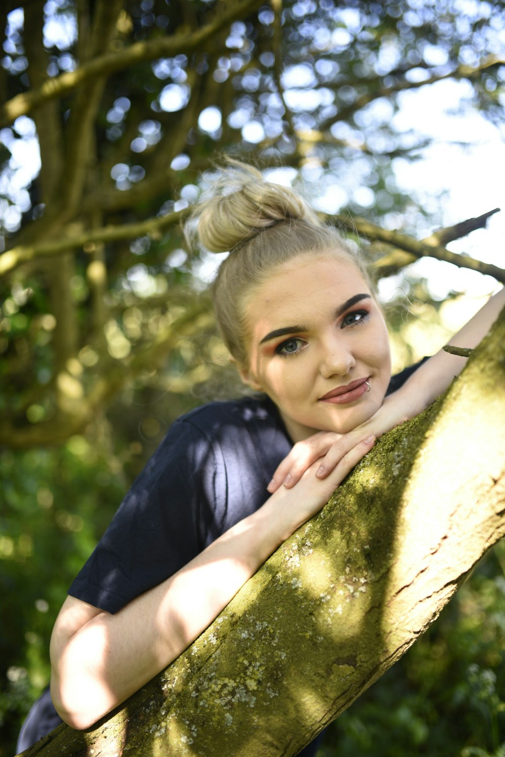 woman in blue crew neck t-shirt leaning on brown tree during daytime