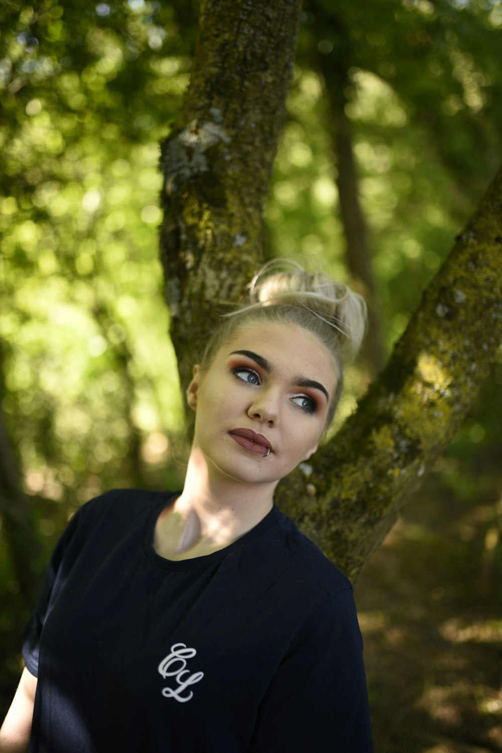 Chica con camisa negra de cuello redondo de pie junto al árbol durante el día