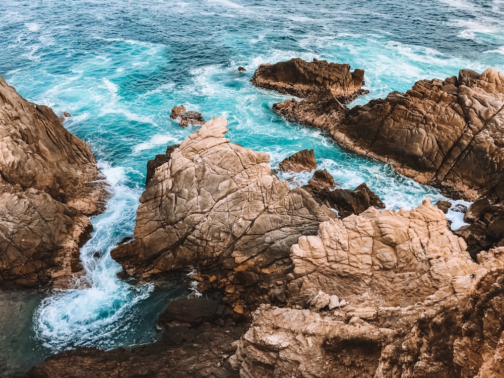 formação rochosa marrom no mar durante o dia