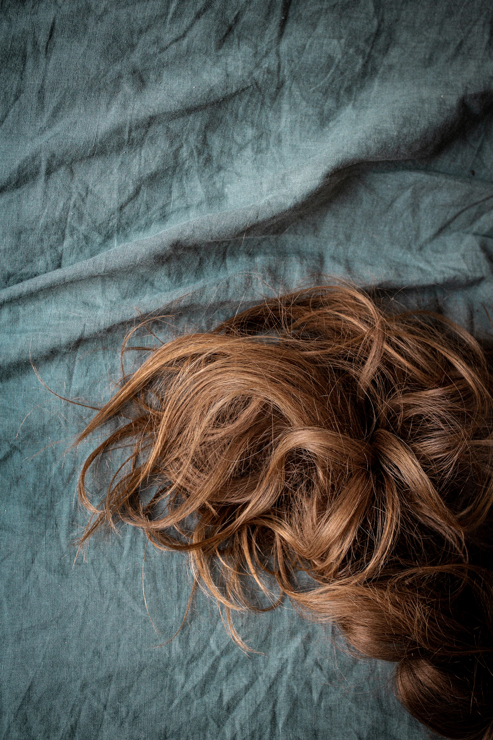 Lengths of brown hair with soft waves laid across blue linen