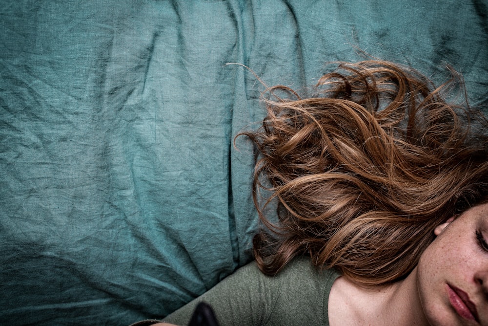 woman in gray shirt lying on blue textile