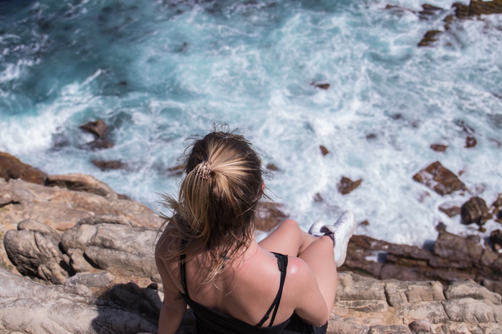 昼間、水辺の近くの岩の上に座る黒いビキニトップの女性