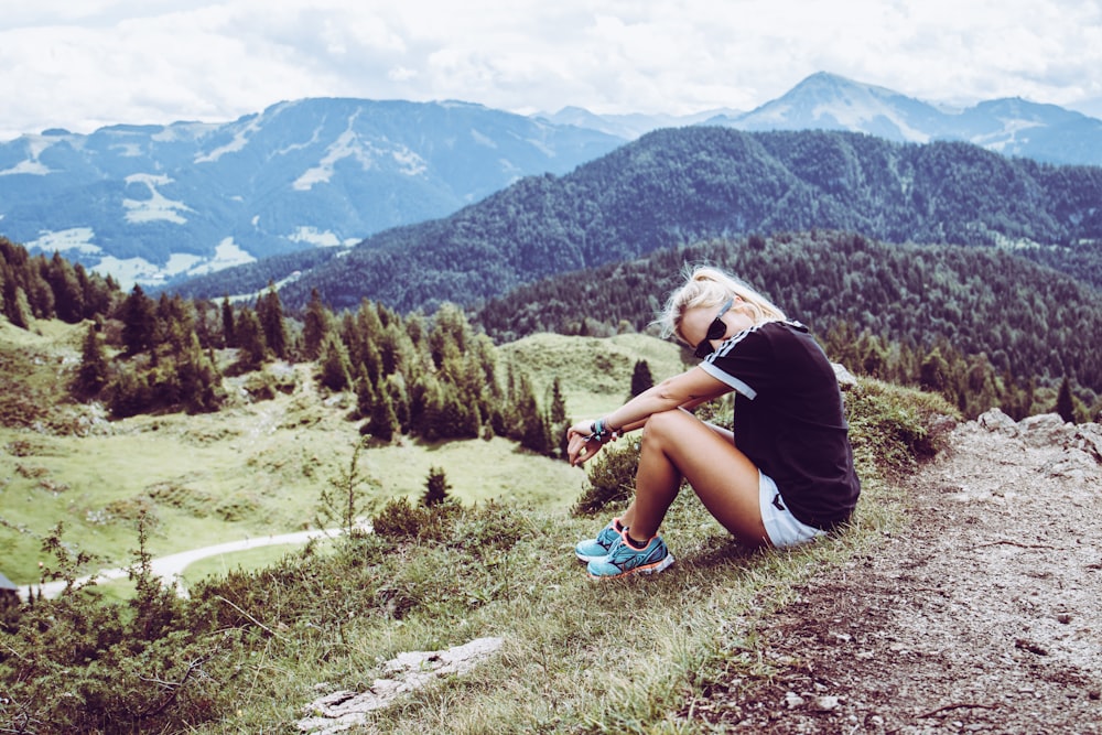 woman in black t-shirt sitting on ground looking at green mountains during daytime