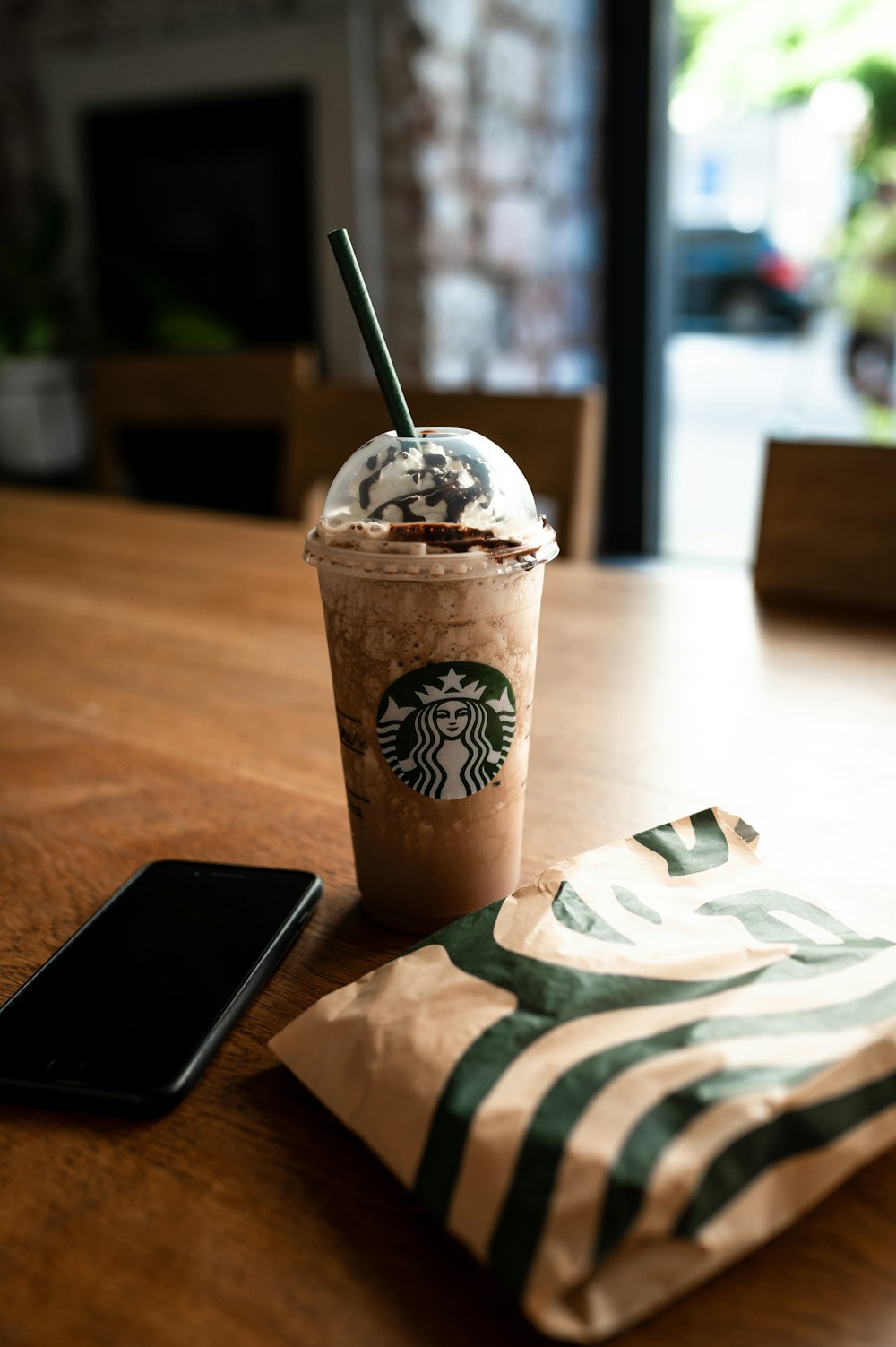 brown and white starbucks cup beside black smartphone on brown wooden table