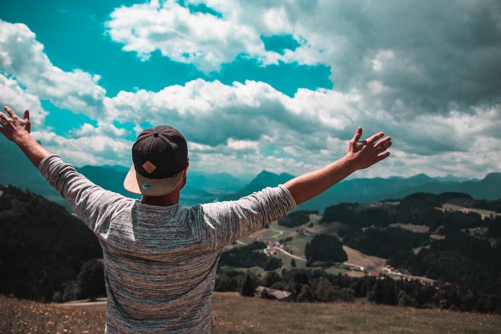 man in grey shirt with black fitted cap raising his hands