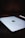 A close-up view of a sleek tablet with a metallic finish, prominently displaying a black apple logo in the center. The device is slightly angled on a dark surface, accompanied by a white stylus placed nearby.