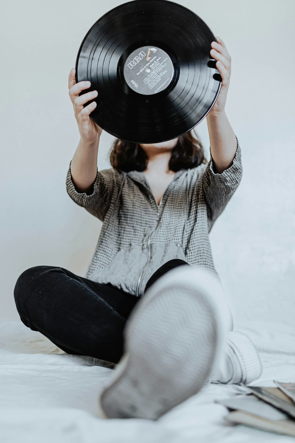 Frau in weißem Strickpullover und schwarzer Hose mit schwarzer Schallplatte
