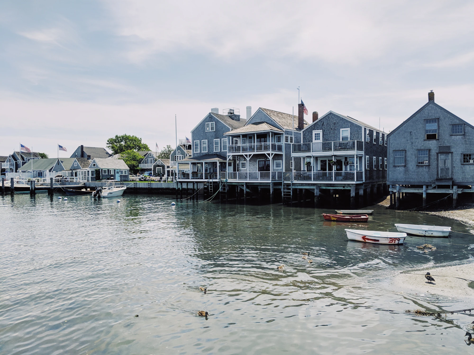 Grey shingled harbor cottages with white trim and porches over the water