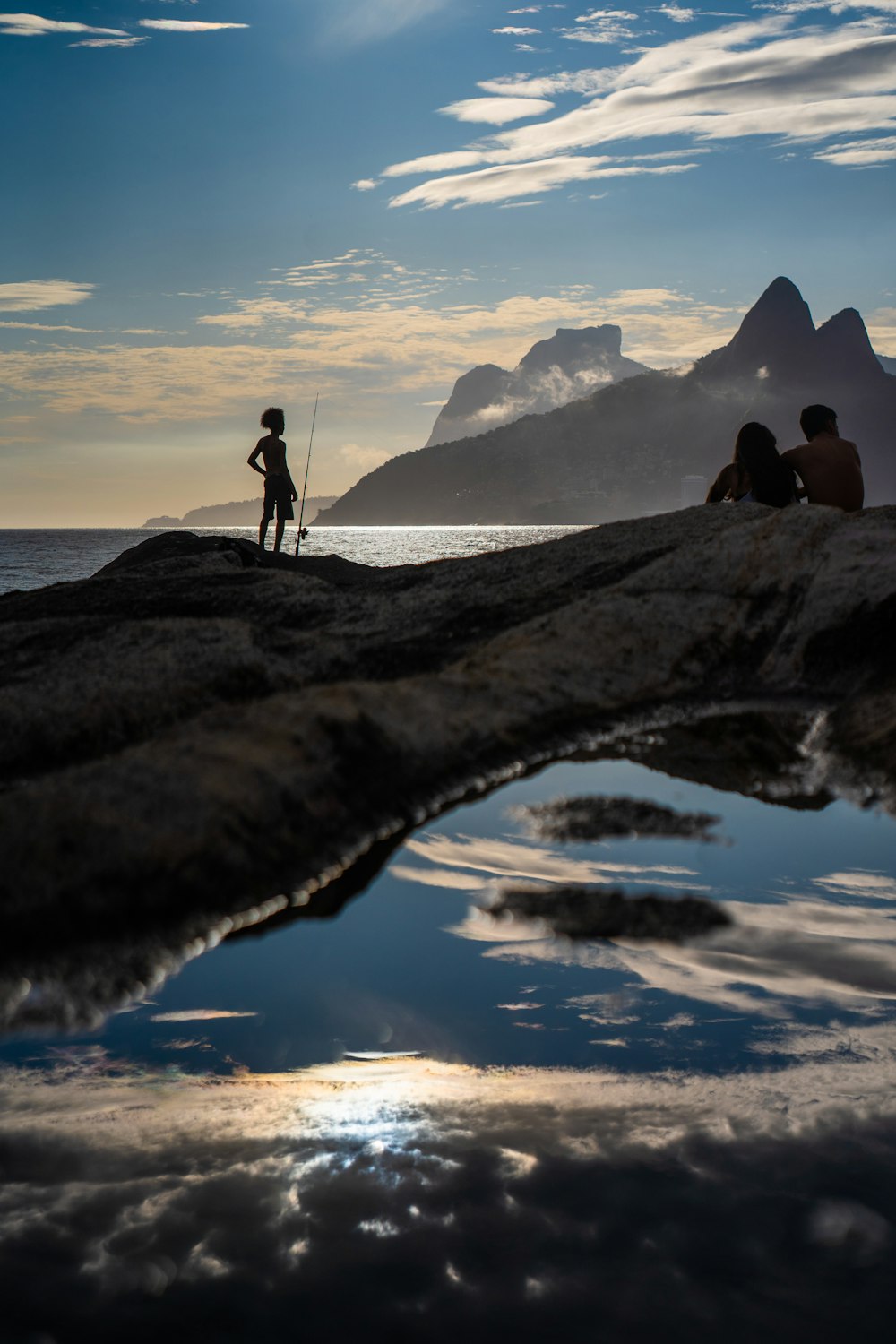 silhouette of 2 person standing on rock formation during sunset