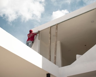 man in red jacket standing on white concrete building under blue and white cloudy sky during