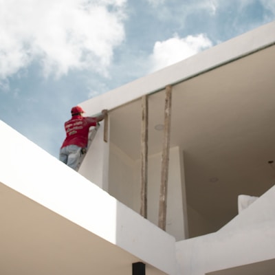 man in red jacket standing on white concrete building under blue and white cloudy sky during