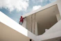 man in red jacket standing on white concrete building under blue and white cloudy sky during