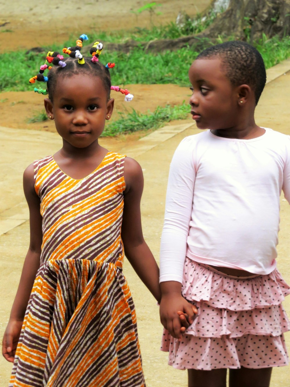 白とオレンジのドレスを着た2人の女の子が昼間、茶色の砂の上に立っている