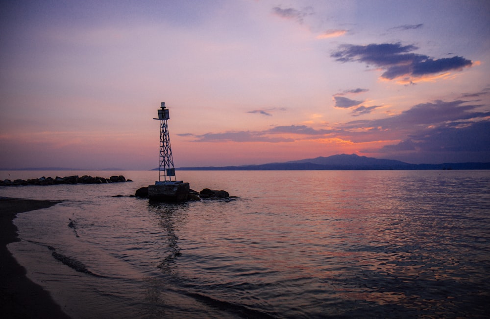 silhouette of person standing on rock in the middle of sea during sunset