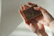 Close-up of a glowing woman gently holding a luxurious black and gold Oria soap bar against a dark background.