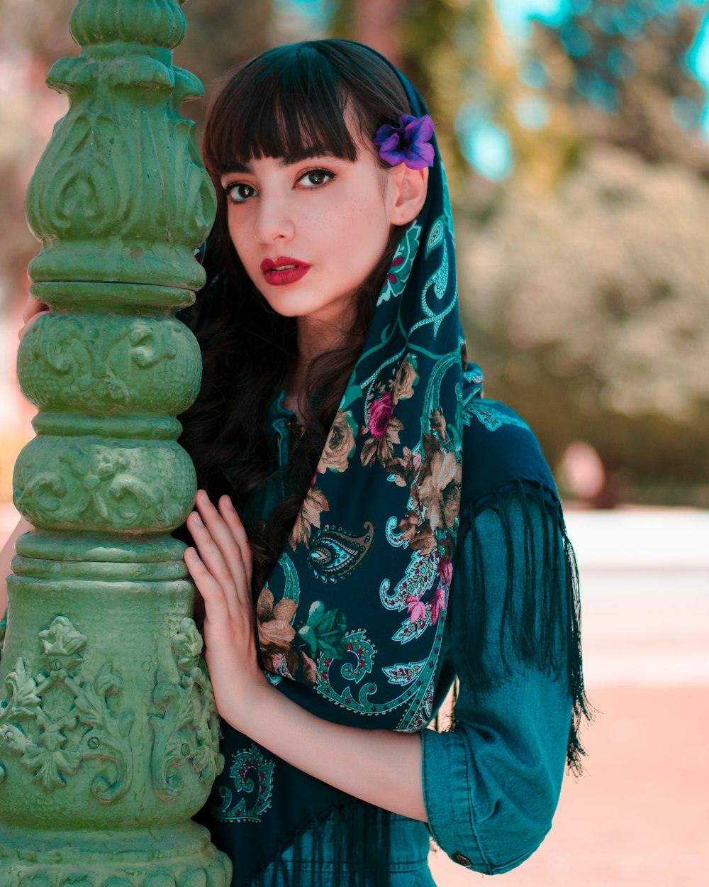 woman in blue and green floral scarf standing beside green concrete post during daytime
