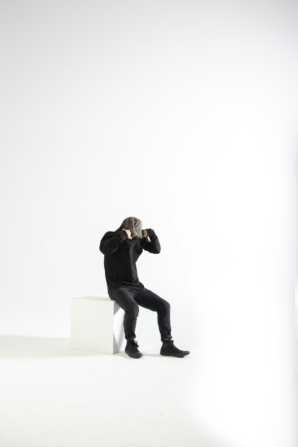 man in black jacket and black pants sitting on white concrete wall