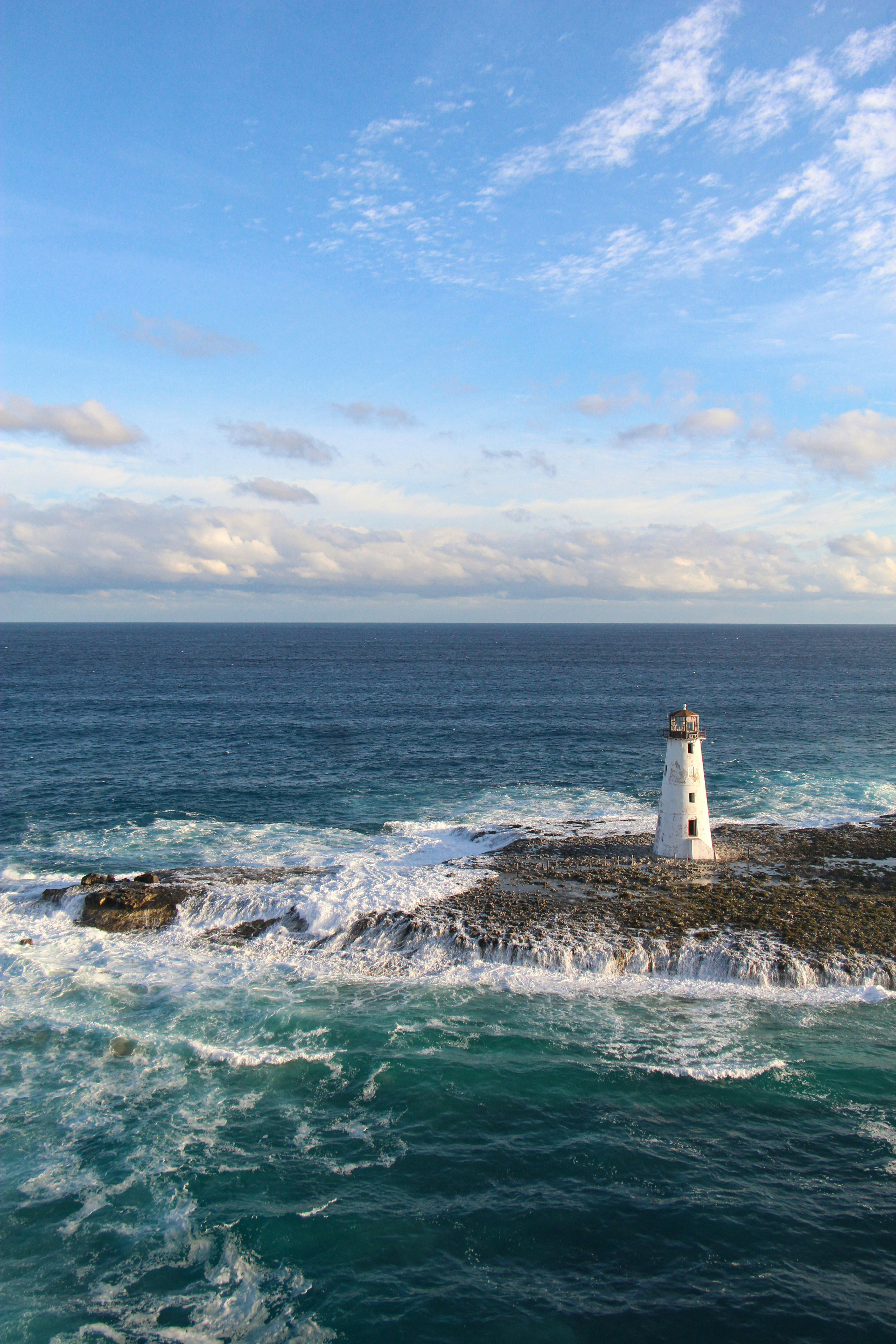 white and brown lighthouse on brown rock formation near body of water during daytime