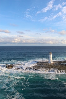 white and brown lighthouse on brown rock formation near body of water during daytime