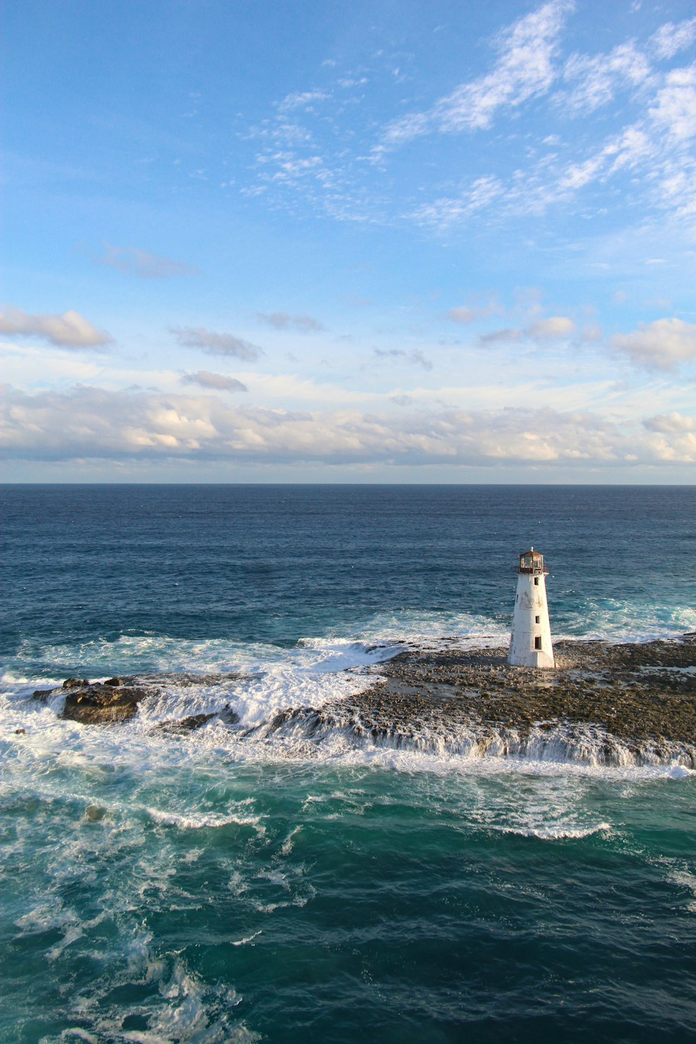 Phare blanc et brun sur une formation rocheuse brune près d’un plan d’eau pendant la journée