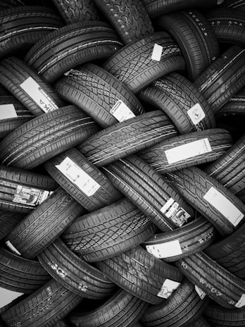 A tightly packed arrangement of new tires, each with distinct tread patterns and labels. The tires are stacked in an overlapping, lattice-like formation, creating an intricate visual texture.
