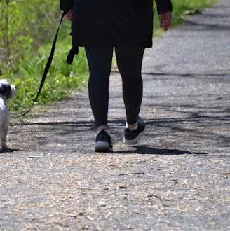 person in red jacket and black pants holding black dog leash