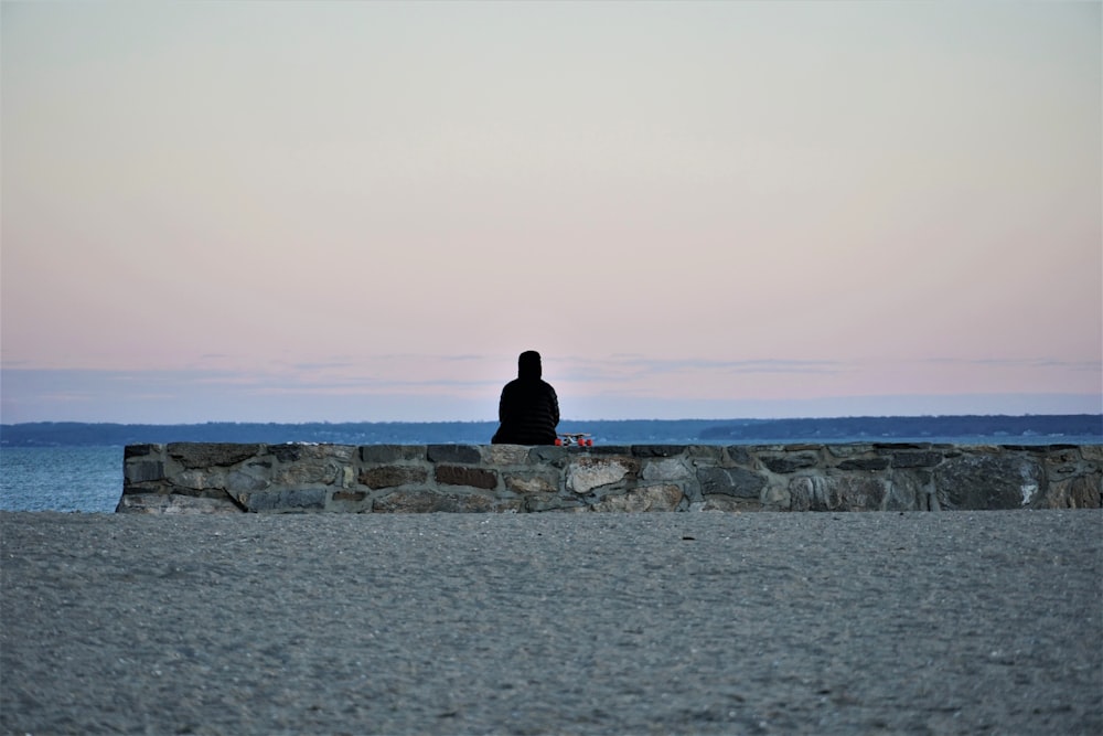 man in black jacket sitting on rock formation near sea during daytime