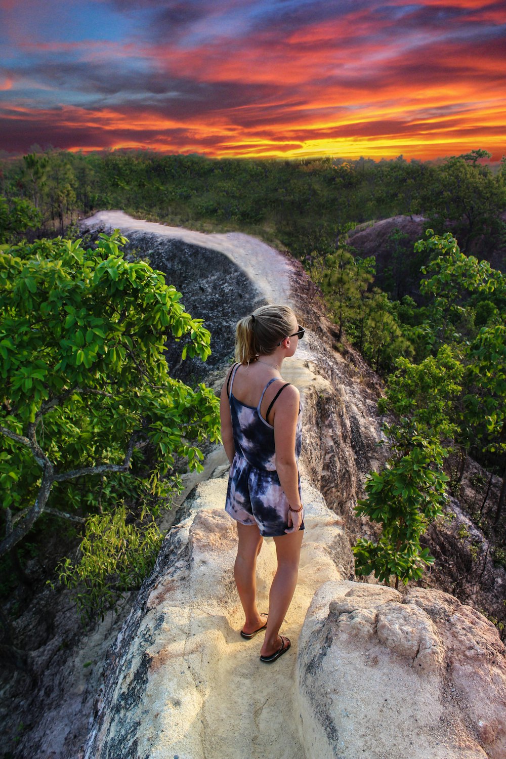 woman in blue and white floral spaghetti strap top standing on brown rock during daytime