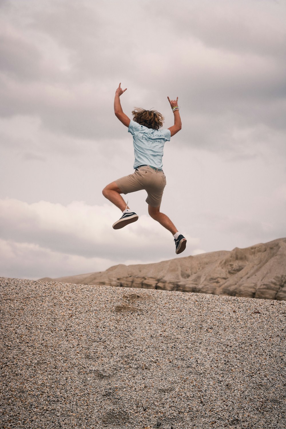 woman in gray shirt and gray shorts jumping on brown sand during daytime