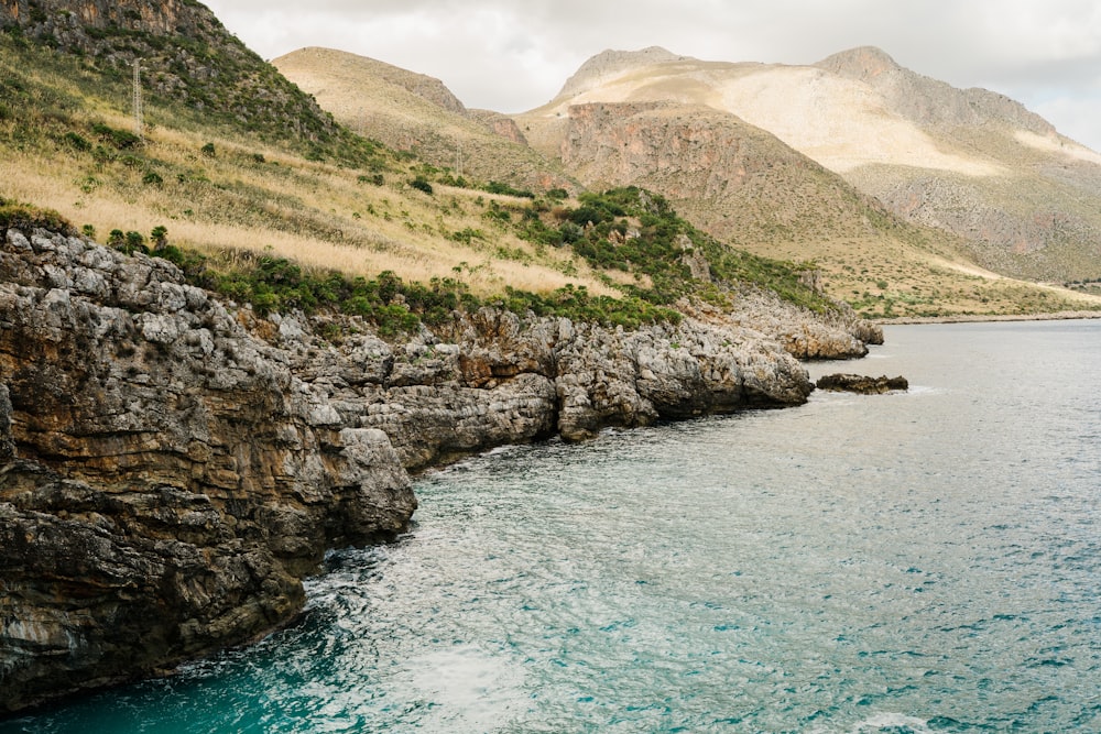 green and brown mountain beside body of water during daytime