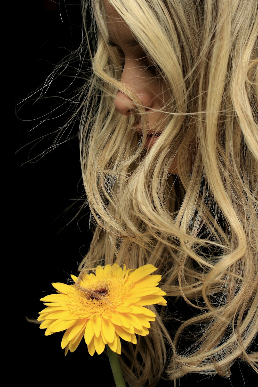 Frau mit blonden Haaren hält gelbe Blume