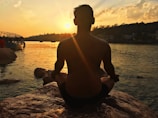 A person meditating by a calm lake at sunrise.