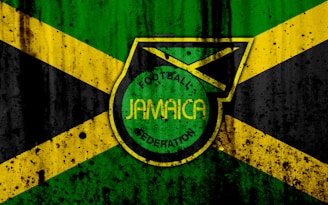 A grunge-style design features the Jamaican flag in the background, with a prominent emblem in the center displaying the words 'Football Jamaica Federation.' The flag consists of green, yellow, and black colors arranged in cross and triangular patterns.
