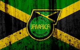 A grunge-style design features the Jamaican flag in the background, with a prominent emblem in the center displaying the words 'Football Jamaica Federation.' The flag consists of green, yellow, and black colors arranged in cross and triangular patterns.