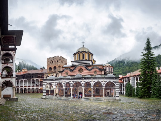brown and beige concrete building near green mountain under white clouds during daytime in Rila Monastery Bulgaria
