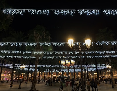 Night view of a lively plaza with string lights and people enjoying live music.