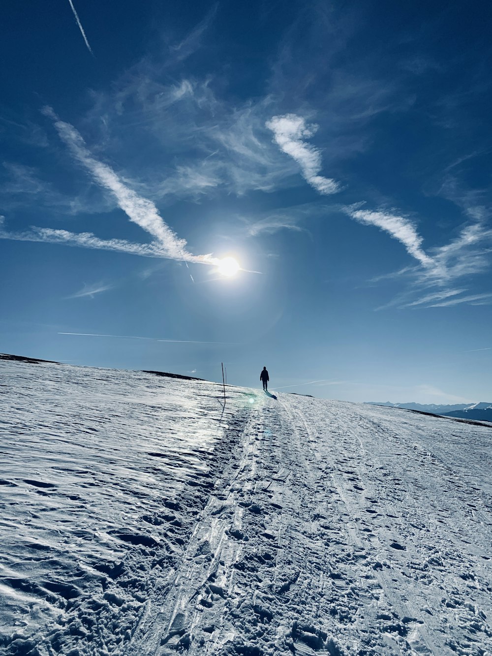 person in black jacket walking on snow covered ground under blue sky during daytime