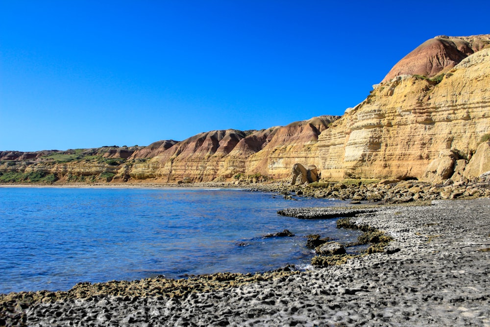 brown rocky mountain beside body of water during daytime