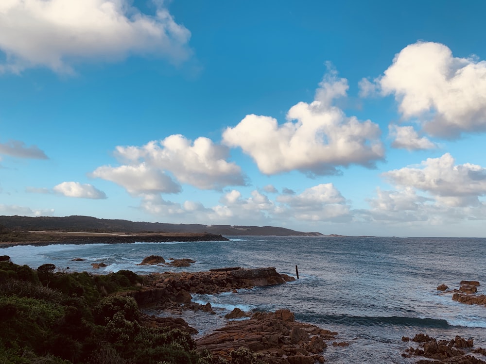 Formazione rocciosa marrone sul mare sotto cielo blu e nuvole bianche durante il giorno