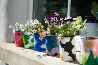 A set of hand-painted ceramic planters with soft floral patterns on a windowsill.