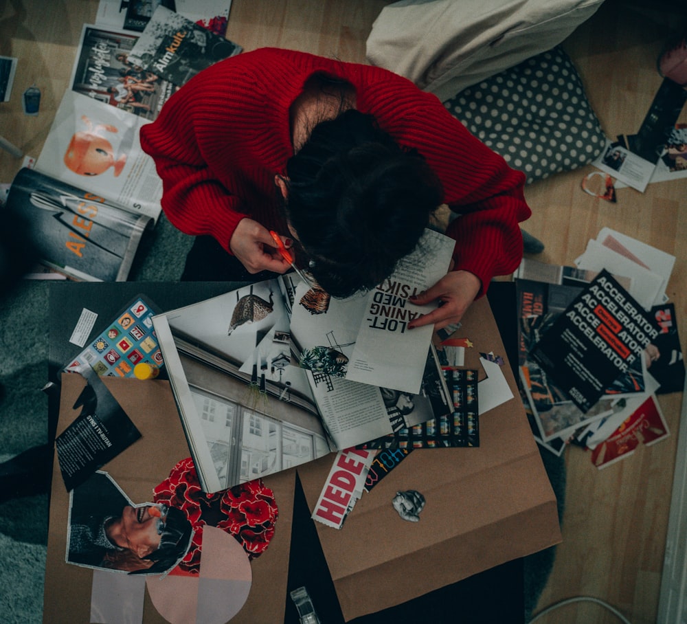 a woman in a red sweater looking down at a pile of books
