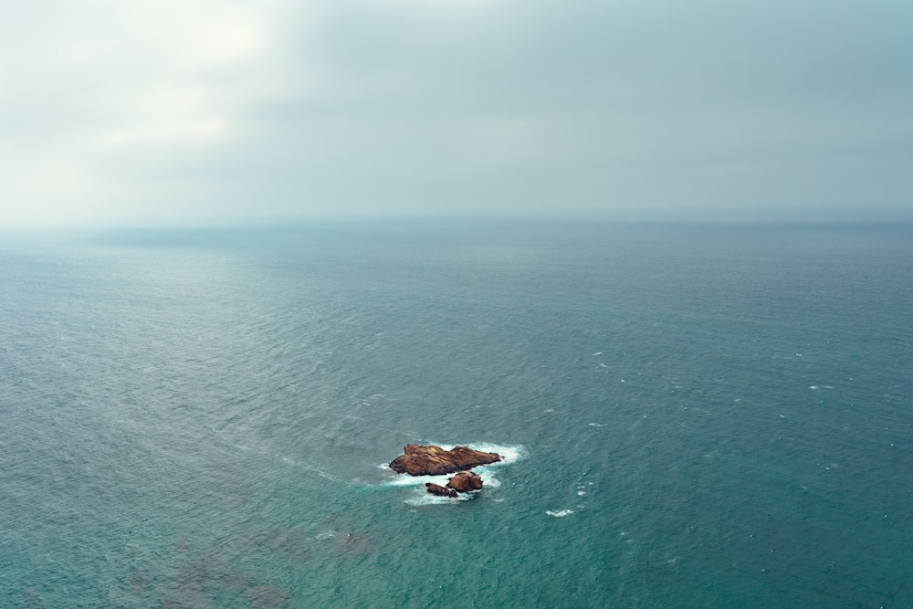 brown rock on blue sea under gray sky