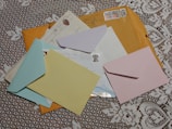 Several colorful envelopes and letters are scattered on a white lace tablecloth. The envelopes include blue, yellow, pink, and brown colors with postal stamps visible on some of them.
