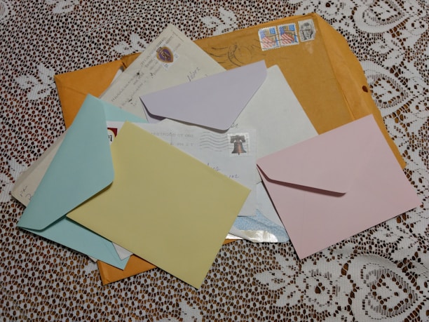 Several colorful envelopes and letters are scattered on a white lace tablecloth. The envelopes include blue, yellow, pink, and brown colors with postal stamps visible on some of them.