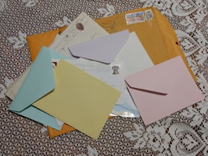 Several colorful envelopes and letters are scattered on a white lace tablecloth. The envelopes include blue, yellow, pink, and brown colors with postal stamps visible on some of them.