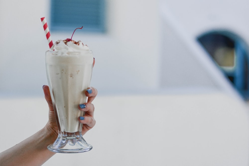 person holding clear drinking glass with white liquid